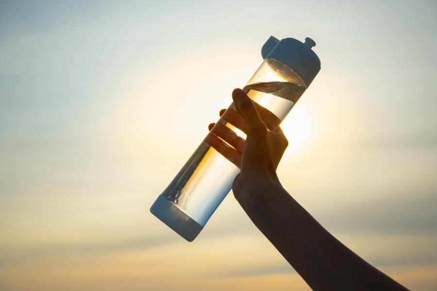 A female hand holds a water bottle up over a summer sky
