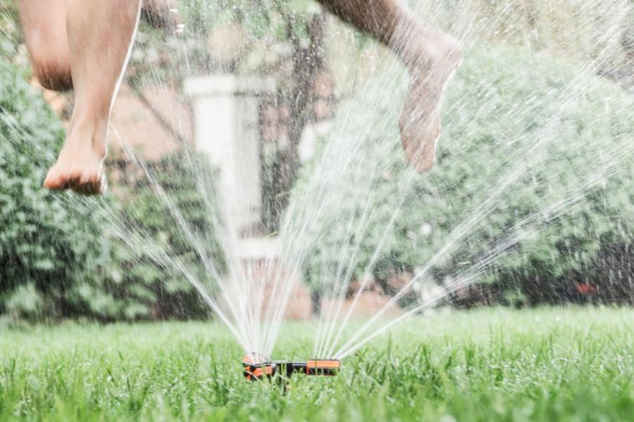 Two kids jump through a lawn sprinkler on a hot summer day